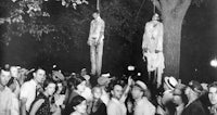 a black and white photo of a group of people hanging from a tree